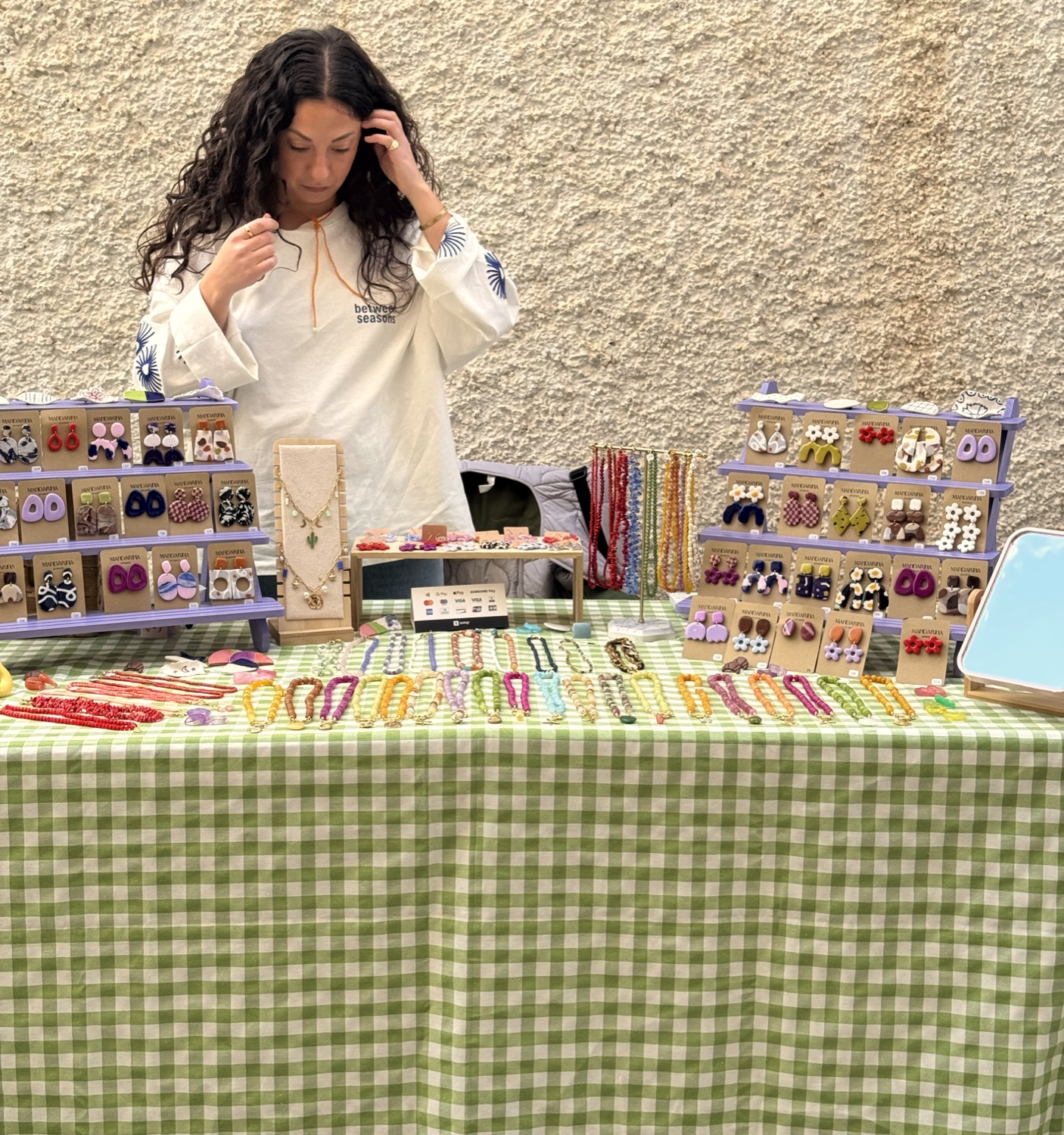 Marina en su puesto de market, con los expositores de pendientes
y los collares sobre un mantel de cuadros verde